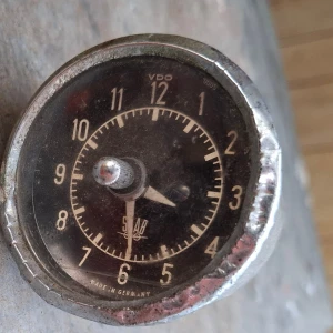 Vintage VDO Saab 95 / 96bilklocka i metall - Säljer en klassisk rund bilklocka från VDO Saab. Klockan har svart urtavla med vita siffror och visare, samt en robust metallram. Mekanismen syns på baksidan med kugghjul och fästen. Perfekt för dig som gillar retroprylar eller samlar på bilaccessoarer. Defekt,renovera eller plocka delar.