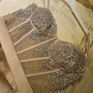 Champagnefärgad långklänning med strass - Supersnygg långklänning i champagnefärg med glittrig överdel täckt av strass och pärlor. Klänningen har smala axelband, markerad byst och en slits framtill. Kjolen är i satinliknande material och faller snyggt. Perfekt för dig som vill sticka ut på bal eller fest! Festklänning i storlek 32/34. Pris kan diskuteras vid snabb affär🤍 är inte kemtvättad - så smutsig nertill klänningen. Samt tyget med pärlor ej helt fast vid dragkedjan, som syns i bilden