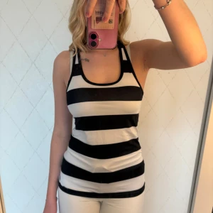 Randig svartvitt träningslinne - Säljer ett snyggt träningslinne med breda svarta och vita ränder. Modellen har brottarrygg och ärmlös design, perfekt för varma dagar eller träning. Materialet känns lätt och stretchigt, vilket gör den superbekväm att bära.