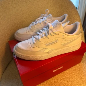 Reebok Club C Revenge vita sneakers storlek 38 - Fräscha Reebok Club C Revenge sneakers i helvitt med diskreta blå detaljer. Klassisk låg modell med rund tå, snörning och platt sula. Tillverkade i syntetmaterial med skinnkänsla och Reebok-logga på sidan. Perfekt för dig som gillar clean och sportig stil.