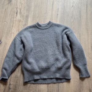 Grå stickad tröja Gina Tricot - Mysig grå stickad tröja från Gina Tricot i storlek M. Tröjan har en rund halsringning och långa ärmar. Materialet är fluffigt och ger en skön känsla, perfekt för kyliga dagar. Enkel och stilren design som funkar till många olika looks.