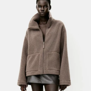 Beige teddyjacka med dragkedja - Säljer en beige teddyjacka med hög krage och två stora fickor framtill. Jackan har en loose passform och stängs med dragkedja. Materialet är mjuk fleece, från H&M såldes förra säsongen i den färgen, jackan är knappt använd