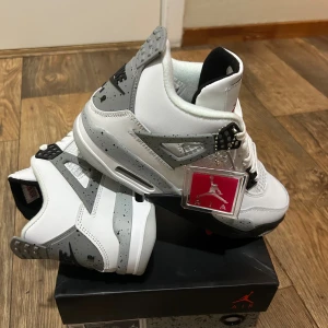 Nike Air Jordan 4 White Cement - Nike Air Jordan 4 White Cement sneakers med vit och grå ovandel i skinn, svarta och röda detaljer samt speckled mönster på gråa partier. Klassisk Jumpman-logga på plösen och häl, snörning och platt sula. Snygg high-top siluett som sticker ut. Om priset inte är passande, så kan det diskuteras 👍