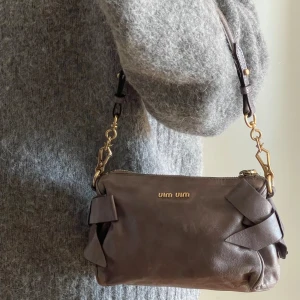 Miu Miu axelväska Vintage - Supersnygg axelväska från Miu Miu i mjukt skinn med dekorativa rosetter på sidorna och guldfärgade metalldetaljer. Väskan har justerbar axelrem och dragkedja upptill. Perfekt storlek för det viktigaste och en stilren look.