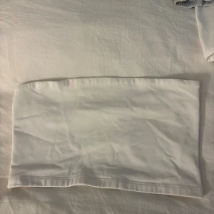 Vit bandeau tubtopp från Gina Tricot - Säljer en enkel och fräsch vit bandeau tubtopp från Gina Tricot i storlek S. Toppen är ärmlös och axelbandslös med en rak och clean design. Materialet är mjukt och stretchigt bomull, perfekt för varma dagar och snygga outfits.