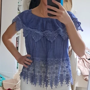 Ljuslila blus med spetsdetaljer - Säljer en ljusblå blus med vackra spetsdetaljer och broderade mönster längs ärmar och nederkant. Blusen har korta ärmar och en lös passform, perfekt för en chill och somrig look. Storlek xs/s