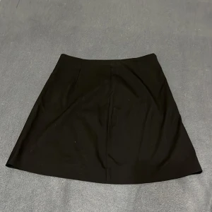 Svart kortkjol från Carin Wester - Stilren svart kortkjol från Carin Wester i modellen Sophia. Kjolen har en klassisk A-linjeform och stängs med dragkedja i sidan. Tillverkad i en mjuk blandning av polyester och viskos som ger en snygg passform och skön känsla.