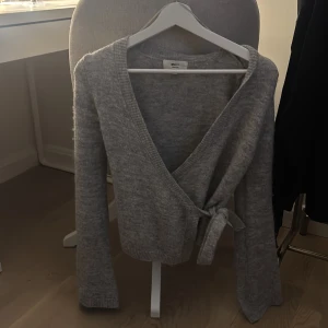 Grå omlottkofta från Gina Tricot - Mysig grå omlottkofta från Gina Tricot i ullblandning perfekt till hösten och vintern🤎🤍 Koftan har lång ärm, v-ringning och knyt i sidan för en snygg passform. Perfekt för lager-på-lager och chill höst- eller vinterdagar.