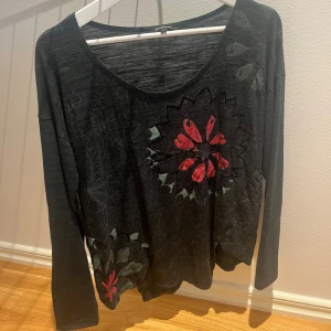 Långärmad topp från Desigual - Grön långärmad topp från Desigual med stora blommiga mönster i rött och grönt framtill. Tunt och mjukt material med lös passform och rund halsringning. Perfekt för dig som gillar unika detaljer och en chill stil.