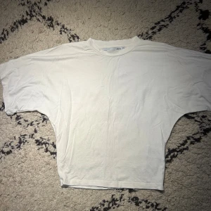 Vit loose t-shirt med breda ärmar - Vit t-shirt i loose fit nedtill och tightare upptill med breda, korta ärmar och rund halsringning. Materialet är mjuk bomull och modellen har en avslappnad siluett som ger en chill vibe. Perfekt för dig som gillar enkel och clean stil.