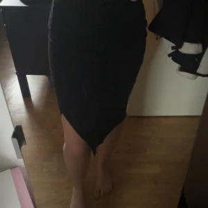 Svart tight långkjol med asymmetrisk kant - Svart långkjol med tight passform och en snygg asymmetrisk nederkant framtill. Kjolen är enkel och stilren, perfekt för dig som gillar minimalistisk stil. Materialet känns mjukt och följsamt mot kroppen.