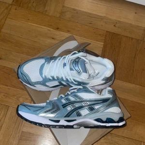 ASICS Gel-Kayano 14 sneakers blå/vit - Säljer ett par ASICS Gel-Kayano 14 sneakers i fräsch vit och ljusblå färg med silvriga detaljer. Skorna har mesh- och syntetmaterial, snörning och en chunky platt sula med gel-dämpning. Perfekt för dig som gillar retrovibbar och sportig stil.