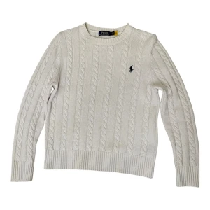 Vit kabelstickad tröja från Polo Ralph Lauren - Vit kabelstickad tröja från Polo Ralph Lauren med klassisk rund hals och broderad logga på bröstet. Tröjan har långa ärmar och ribbade muddar vid ärmslut och nederkant. Perfekt för dig som gillar stilrena och tidlösa plagg. Pris kan diskuteras!
