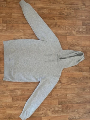 Grå hoodie från Smog med huva - En stilren grå hoodie från Smog i storlek M. Tröjan har en klassisk huva med snörning och långärmade ärmar. Materialet är mjukt och känns skönt mot huden, perfekt för chill dagar. Regular fit som sitter snyggt utan att vara för tight.
