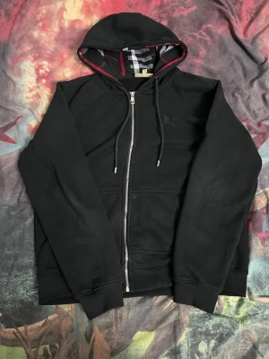 Burberry hoodie - Svart Burberry hoodie med klassiskt rutigt mönster i huvan och insidan. Tröjan har broderad Burberry-logga på bröstet. Den har mjuk bomull på insidan som håller dig varm speciellt nu i vintern. Den sitter som storlek M. Självklart tvättas den innan de fraktas. Skriv gärna om du vill diskutera priset!