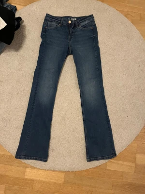 Blå bootcut jeans från Denim 1953 - Snygga blå jeans från Denim 1953 i storlek 36 med klassisk bootcut passform. Jeansen har fem fickor, dragkedja och knapp framtill samt detaljer i kopparfärg. Materialet är jeans med lätt tvättad look och utsvängda ben. Har aldrig använts! Skriv bara om ni vill ha mått eller fler bilder!🩵