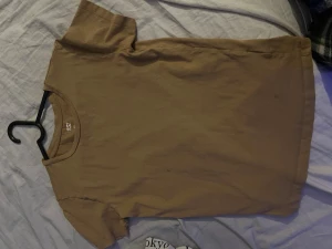 Beige t-shirt från 157 - En enkel och stilren beige t-shirt från 157 i storlek L. T-shirten har rund hals och korta ärmar, perfekt för dig som gillar basic och neutrala färger. Materialet känns mjukt och skönt mot huden, troligtvis bomull. Passar dig som vill ha en clean look.