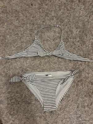 Vit och marinblå randig bikini H&M - Snygg bikini från H&M med vita och marinblå ränder. Överdelen har knyt i nacken och en rosett framtill, medan underdelen har knyt i sidorna