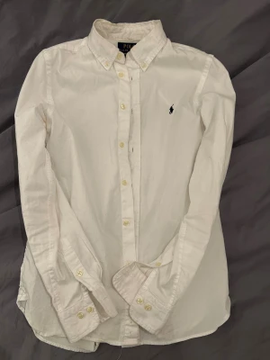 Vit skjorta Polo Ralph Lauren slim fit - Vit skjorta från Polo Ralph Lauren i slim fit-modell. Klassisk button-down krage, långa ärmar med manschettknappar och broderad med Ralph Lauren logga på bröstet. Tillverkad i mjuk bomull, perfekt för en clean och stilren look. Perfekt för julen! Strl 16 OBS skriv till mig innan köp.