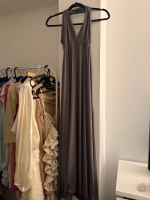 Lång grå klänning med öppen rygg - Långklänning i mjukt grått tyg med djup v-ringning och breda axelband. Klänningen har öppen rygg och ett snyggt fall. 