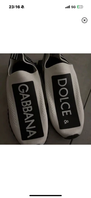 Dolce & Gabbana vita sneakers - Säljer ett par vita Dolce & Gabbana sneakers med svart och vit logga på ovansidan och hälen. Skorna har en chunky platt sula och är tillverkade i stickad syntet med elastisk passform. Snygg och modern design som sticker ut med stora tryckta bokstäver.