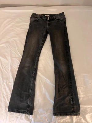 Bootcut jeans från Gina Tricot, svart - Svarta bootcut jeans från Gina Tricot i storlek 158. Snygg tvätt med lätt slitning, klassisk femficksmodell och dubbla silverknappar framtill. Jeansen har normal passform och är tillverkade i jeansmaterial med stretch.