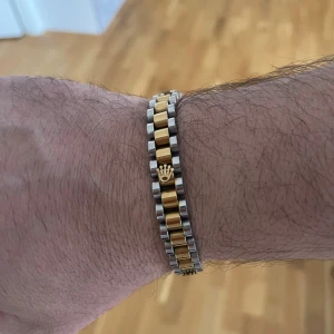 tvåfärgat armband i metall - Snyggt armband från  i klassisk tvåfärgad design med guld- och silverlänkar. Armbandet har den ikoniska kronan i guld på flera ställen och en robust, fyrkantig form. Perfekt för dig som gillar exklusiva detaljer och stilren look.