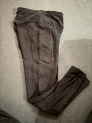 Svarta träningstights  med fickor - Svarta träningstights med hög midja och praktiska fickor på sidorna. Snygga sömmar och stretchigt material som sitter tight och bekvämt med fickor på sidan. Perfekta för träning eller chill. Liten logga i vitt bak på linningen.