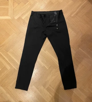 Svarta kostymbyxor Riley Stanton - Snygga svarta kostymbyxor från Riley Stanton med klassisk rak passform. Byxorna har diskreta fickor och stängs med knappar och dragkedja. Byxorna är både stilrena och bekväma. Perfekta för en dressad look.