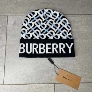  mössa med mönster av märket burberry - Snygg mössa med stor vit logga framtill och ett grafiskt mönster i svart, vitt och ljusblått. Mössan är stickad och har en uppvikt kant. Perfekt för dig som vill ha en trendig accessoar med lyxig känsla.