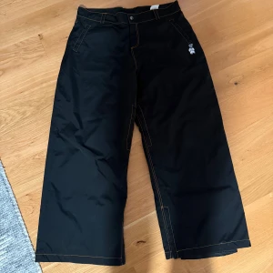 Harlaut Apparel Shit Kids | XL - Ett par svarta skidbyxor från Harlaut Apparel i XL.  Med orangefärgade sömmar. Byxorna har en broderad detalj på ena bakfickan och en liten logotyp på framsidan. Använda 1 säsong. | Byte mot typ capeesh eller harlaut jacka kan vara intressant|