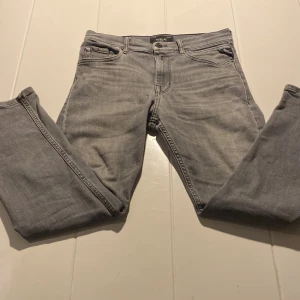 Grå Replay jeans, rak modell - Snygga grå jeans från Replay med klassisk femficksdesign och svarta detaljer på bakfickorna. Jeansen har rak passform och är tillverkade i mjukt jeanstyg som sitter skönt. Perfekt för dig som gillar stilrena och tidlösa jeans.