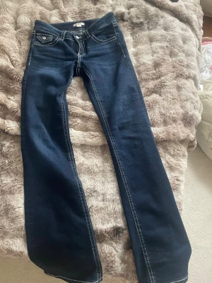 Mörkblå bootcut jeans med kontrastsömmar - Snygga mörkblå jeans med bootcut passform och låg midja från Gina tricot yung i storlek 164 , passar som xs. Jeansen har tydliga vita kontrastsömmar, klassiska fickor fram och bak med lock och knappdetaljer. Materialet är jeans och de sitter riktigt bra på kroppen.