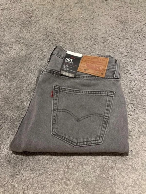 Gråa Levi's 501 jeans  - Säljer ett par helt nya och oanvända gråa Levi's 501 jeans i klassisk straight fit. Jeansen är tillverkade i 100% bomull och har normal midja, fem fickor och ikonisk läderpatch bak. Perfekt för dig som gillar en tidlös och clean look.