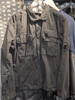 C.P. Company - Obetydligt använd.Svart overshirt från C.P. Company med klassisk krage, stora bröstfickor med lock och tryckknappar samt ikonisk linsdetalj på ärmen.  https://www.casualbasement.com/products/gabardine-lens-utility-shirt
