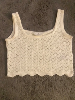 Vit stickad linnetopp från H&M - Supersöt vit stickad linnetopp från H&M med breda axelband och ett snyggt hålmönster över hela toppen. Den har en vågig kant nertill som ger en extra detalj. Perfekt för varma dagar och enkel att styla med jeans eller kjol.