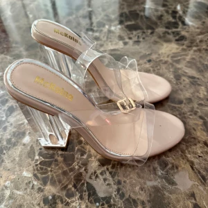 Klara klackskor från McKeline - Säljer ett par trendiga klackskor från McKeline med transparent rem och blockklack i akryl. Skorna har en beige sula och öppen tå, vilket ger en modern och stilren look. Perfekta för dig som vill sticka ut med en cool och minimalistisk vibe.