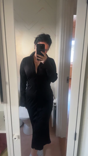 Svart lång skjortklänning - Säljer en svart lång skjortklänning med knappar framtill och krage. Klänningen har lång ärm och en figurnära passform som ger en snygg siluett. Perfekt för dig som gillar stilrena och klassiska plagg med edge. Har även en likadan i st 38 