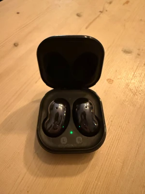 Samsung Galaxy Buds Live - Samsung Galaxy Buds Live trådlösa hörlurar med laddningsetui. Unik bönformad design, aktiv brusreducering och lång batteritid. Svart färg, komplett med originaletui. Mindre yttre slitage syns på etuiet, men hörlurarna är i gott skick och fungerar utmärkt.