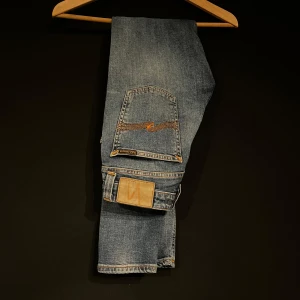 Blå jeans från Nudie Jeans - Snygga blå jeans från Nudie Jeans med klassisk femficksdesign och orange sömmar. Jeansen har en normal passform. Perfekta för en avslappnad stil. Storlek 27 32
