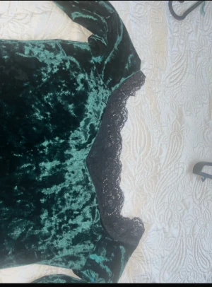 klänning - Mörkgrön sammetsklänning med långa ärmar och snygga svarta spetsdetaljer vid halsringning och nederkant. Klänningen har en figurnära passform och känns både lyxig och trendig med sitt mjuka material och eleganta look.