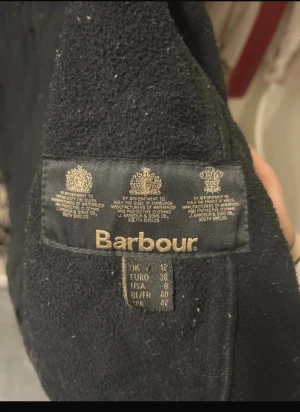 Svart quiltad jacka från Barbour - Säljer en svart quiltad jacka från Barbour International med snygga guldiga knappar och dragkedja. Jackan har flera fickor framtill, hög krage och klassisk Barbour-patch på bröstet. Perfekt för dig som vill ha en stilren och tidlös look.