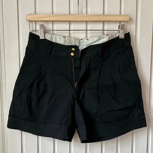Välskräddade shorts från Noa Noa - Svarta korta shorts från Noa Noa i storlek XS med hög midja och fickor. Dubbla små gula knappar fram och en bakficka med knapp ger en unik detaljkänsla som är typiskt för Noa. Välskräddat bommulsmaterial med tidlöst klassiskt snitt. Superfin kvalitet. 