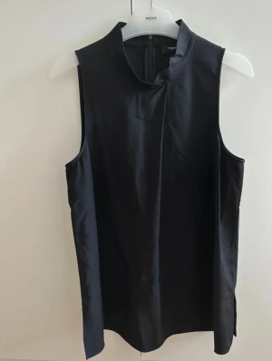 Svart polotopp från Theory - Stilren svart polotopp från Theory med ärmlös design och rak passform. Toppen har en hög krage, diskret slits i sidan och dragkedja bak. Materialet är mjukt och har en lätt glansig finish som ger en modern och exklusiv känsla