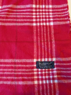 Rutig röd halsduk från Burberrys - Snygg rutig halsduk från Burberrys i rött och vitt, tillverkad i 100% lammull. Klassisk design med fransar i ändarna och tydlig Burberrys-label. Perfekt att slänga över axlarna för en cool och tidlös look.