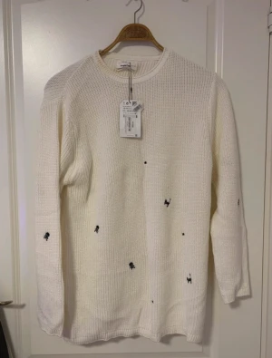 Vit stickad tröja med svarta symboler - But stickad tröja från med svarta broderade små symboler