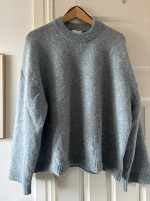 Stickad tröja från H&M - Mycket bra skick! Blågrå oversized stickad tröja från H&M i mohair- och ullblandning. Tröjan har bred ribbad mudd i halsringning, ärmslut och nederkant samt långa ärmar med lös passform. 