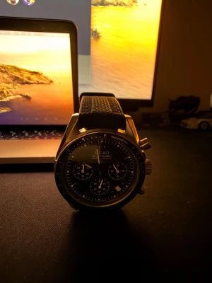 Seiko Speedmaster-Moonswatch svart/silver - Säljer en Seiko Speedmaster kronograf med svart urtavla och silverfärgat stålboett. Klockan har flera subdials, den ikoniska tachymeter och datumfunktion. Baksidan har en cool gravyr med månmotiv och rymdfarkost, som OMEGA Speedmaster. Svart syntetarmband med textur för extra stil. Armbandet i sig kostar 800kr och inköpspris på allt är 4000kr. Billigare pris lm ni vill hämta, finns att hämta på Östermalm.