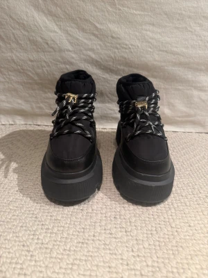 Inuikii Endurance puffer boots size 40 - Helt oanvända! Varma vinterboots med (6cm hög) rejäl sula och gosig, mjuk och varm shearling-päls inuti.  Storlek 40.  Retail price: 500EUR  ABOUT:  Discover the perfect blend of tech and glam with our new «Endurance Puffer» — an urban explorer's essential. Easily customized with an adjustable drawstring, it effortlessly combines style and function, showcasing INUIKII's commitment to timeless yet practical design.   Materials Outer material: 60% polyester, 40% leather Upper lining: 100% shearlin