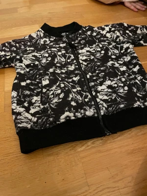 Svartvit bomberjacka från Firefly - Säljer en svartvit bomberjacka från Firefly med blommigt mönster. Jackan har ribbade muddar, dragkedja framtill och två fickor. Perfekt för dig som gillar coola prints och vill sticka ut lite extra.